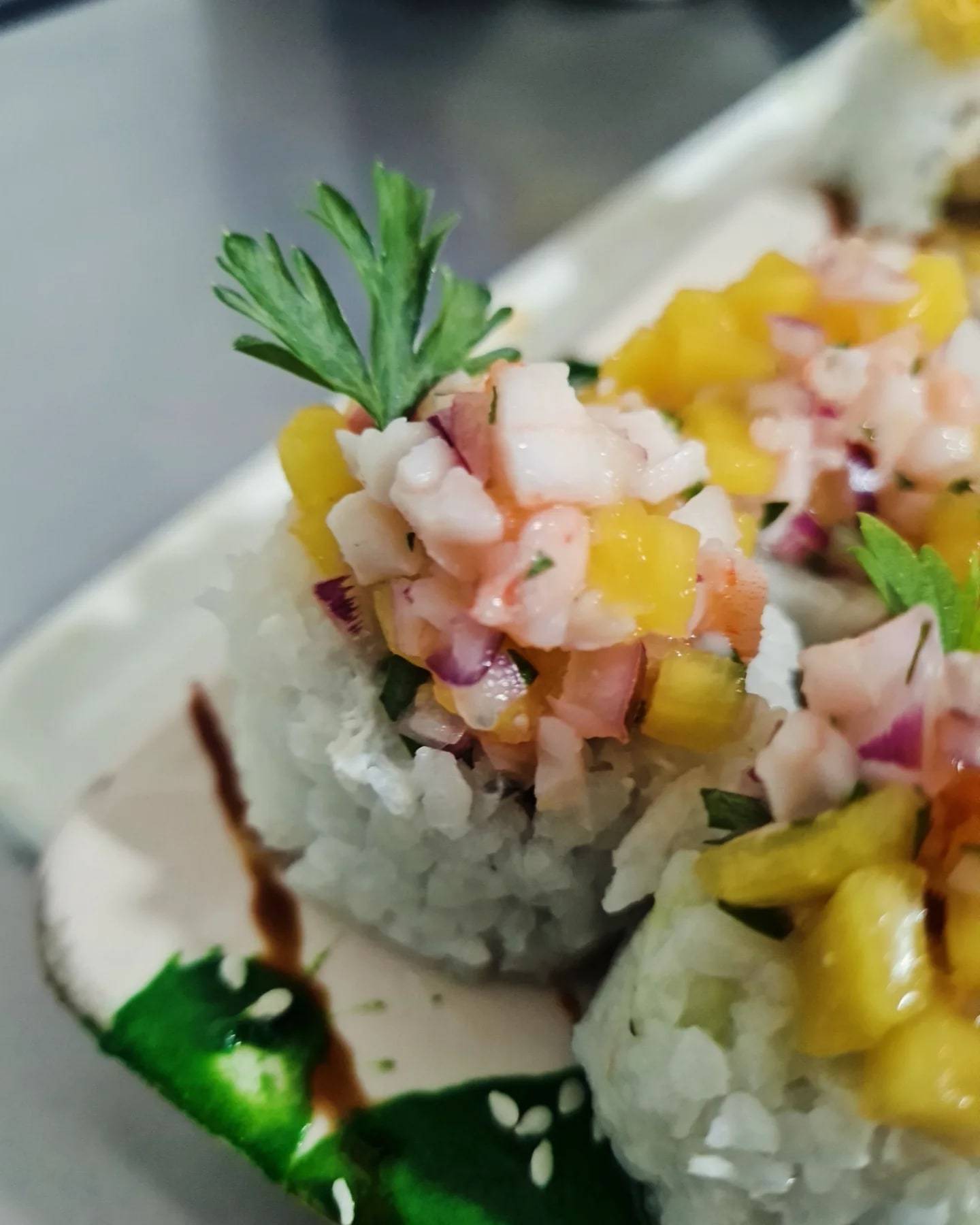 Piezas de sushi coronadas con un tartar de langostinos, mango y cebolla morada, con hojas de perejil